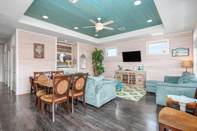 living room featuring dark hardwood / wood-style flooring, a raised ceiling, ceiling fan, and wood walls