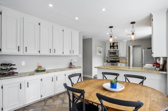 kitchen with white cabinetry, hanging light fixtures, stainless steel appliances, light stone counters, and a textured ceiling