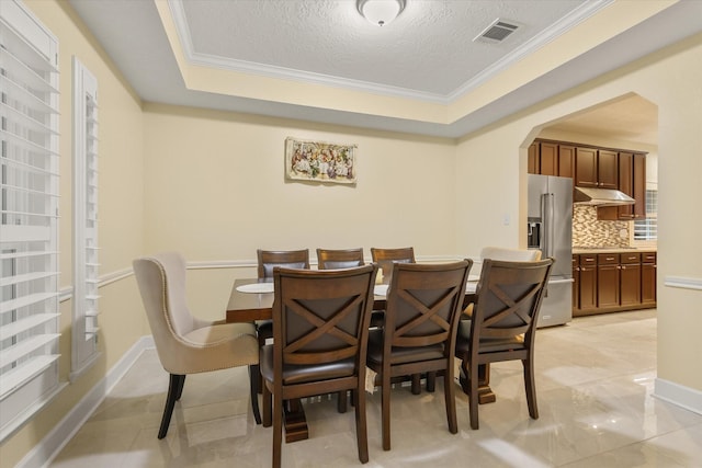 dining room featuring a raised ceiling, a textured ceiling, and ornamental molding