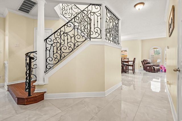 staircase featuring a textured ceiling, ornate columns, and crown molding