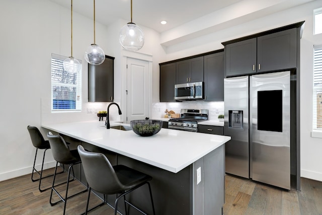 kitchen featuring a breakfast bar, sink, appliances with stainless steel finishes, decorative light fixtures, and dark hardwood / wood-style flooring