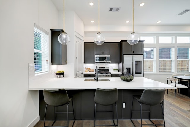 kitchen with hardwood / wood-style floors, sink, hanging light fixtures, a breakfast bar area, and stainless steel appliances