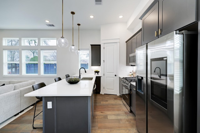 kitchen with pendant lighting, a center island with sink, a kitchen breakfast bar, dark hardwood / wood-style floors, and appliances with stainless steel finishes