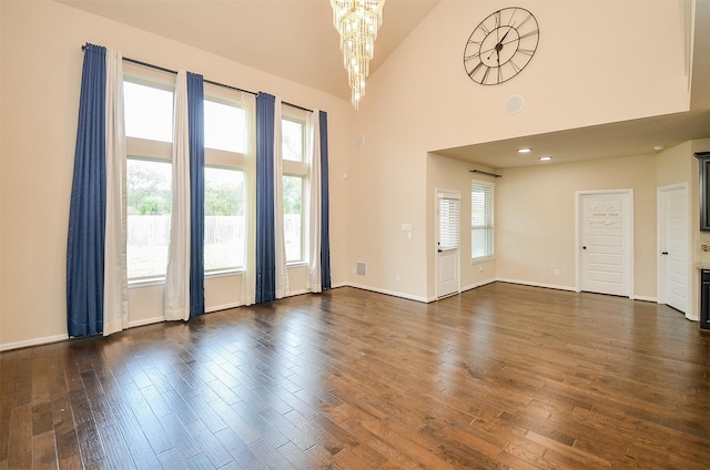 spare room with high vaulted ceiling, dark hardwood / wood-style floors, an inviting chandelier, and a healthy amount of sunlight