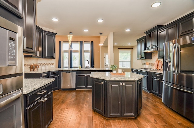 kitchen with light stone countertops, appliances with stainless steel finishes, decorative backsplash, dark wood-type flooring, and a kitchen island