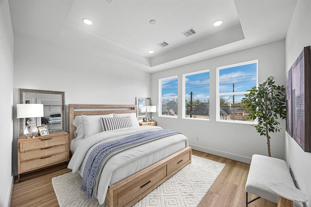 bedroom with light hardwood / wood-style floors and a raised ceiling