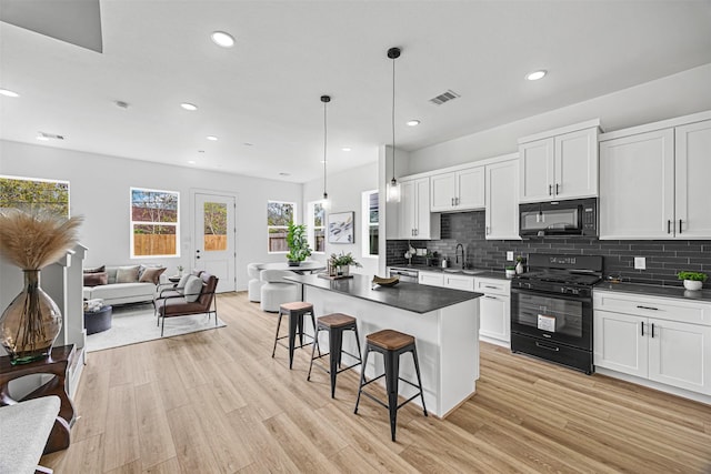 kitchen featuring pendant lighting, black appliances, white cabinetry, sink, and a breakfast bar area