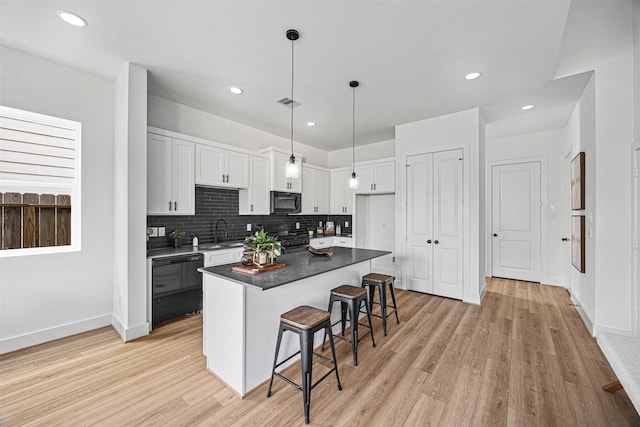 kitchen featuring decorative light fixtures, a center island, black appliances, a breakfast bar area, and white cabinets