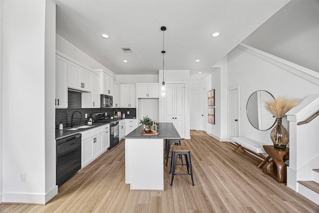 kitchen featuring hanging light fixtures, black appliances, white cabinets, a breakfast bar, and a center island