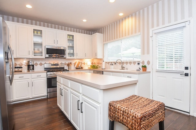 kitchen with white cabinets, appliances with stainless steel finishes, a kitchen island, dark wood-type flooring, and sink