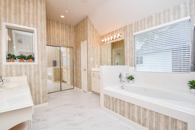 bathroom featuring vaulted ceiling, a relaxing tiled tub, and vanity