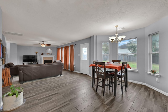 dining area featuring ceiling fan with notable chandelier, a textured ceiling, dark hardwood / wood-style flooring, and a healthy amount of sunlight