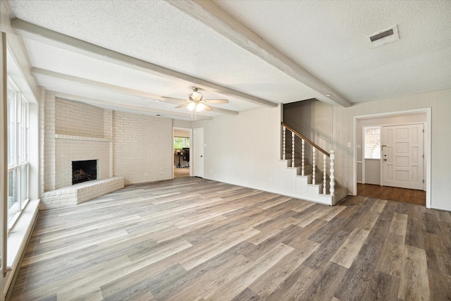 unfurnished living room with ceiling fan, beamed ceiling, a healthy amount of sunlight, and hardwood / wood-style flooring