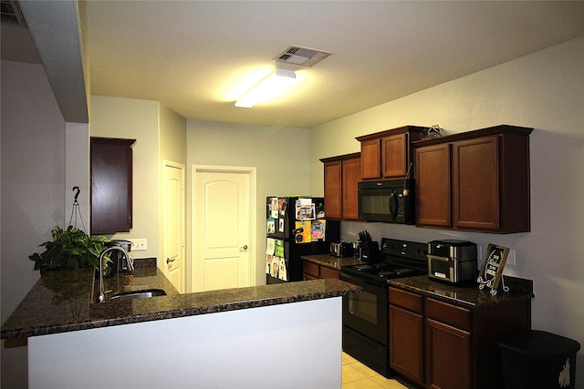 kitchen featuring sink, kitchen peninsula, dark stone counters, light tile patterned floors, and black appliances