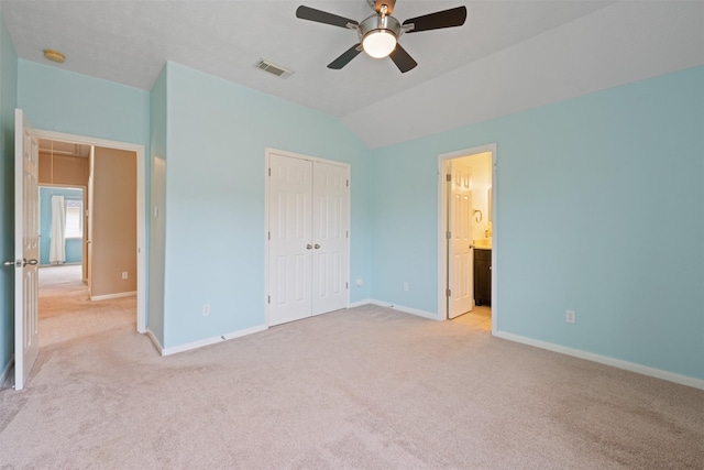 unfurnished bedroom featuring ceiling fan, ensuite bathroom, lofted ceiling, light carpet, and a closet