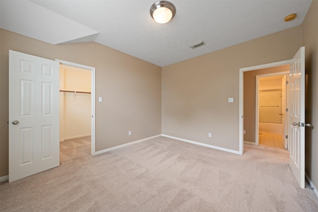 unfurnished bedroom featuring a spacious closet, a closet, light carpet, and lofted ceiling