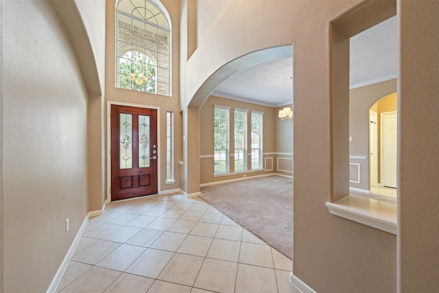 foyer entrance with light carpet, crown molding, a towering ceiling, and a chandelier