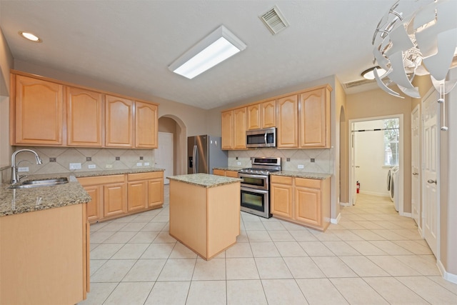 kitchen featuring sink, stainless steel appliances, light stone counters, backsplash, and a kitchen island