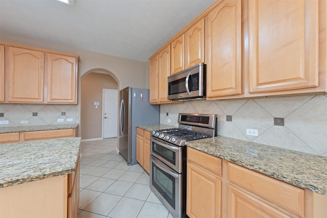 kitchen with decorative backsplash, light brown cabinetry, light stone counters, stainless steel appliances, and light tile patterned flooring