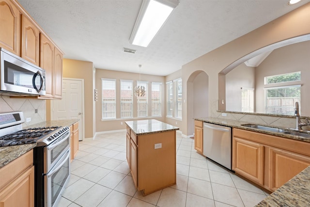 kitchen with stainless steel appliances, a kitchen island, a wealth of natural light, and light stone counters