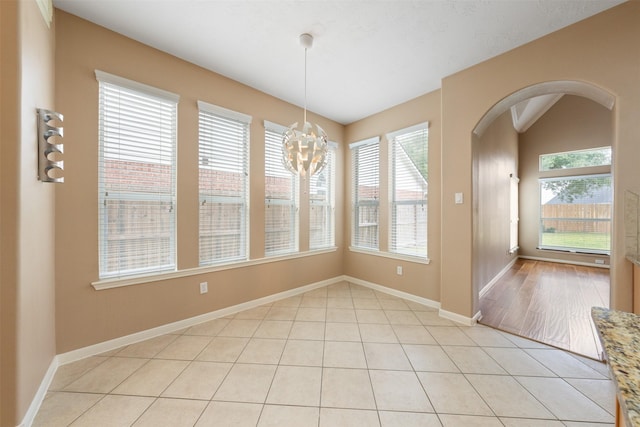 unfurnished dining area featuring light tile patterned floors, a healthy amount of sunlight, and an inviting chandelier