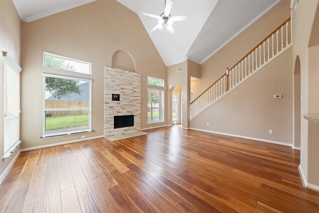 unfurnished living room featuring a wealth of natural light, a stone fireplace, wood-type flooring, and high vaulted ceiling