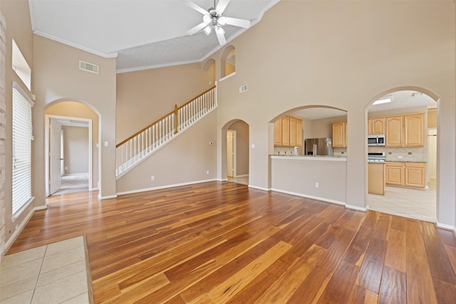 unfurnished living room featuring ceiling fan, light wood-type flooring, ornamental molding, and a high ceiling