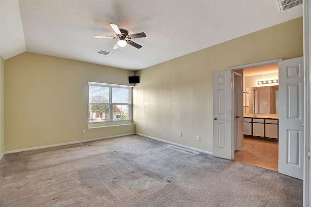 spare room with a textured ceiling, light colored carpet, vaulted ceiling, and ceiling fan