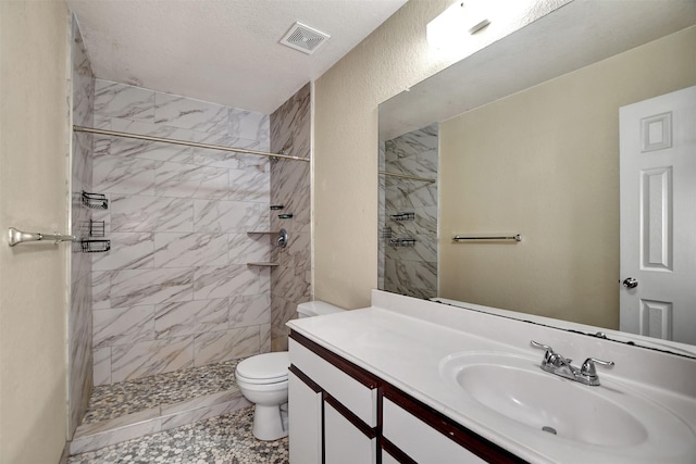 bathroom with a tile shower, vanity, a textured ceiling, and toilet