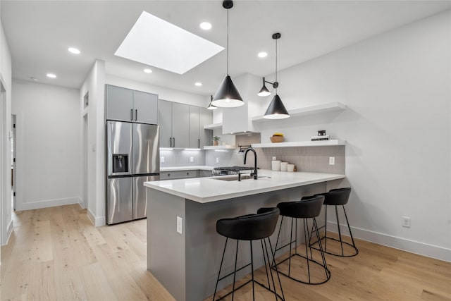 kitchen with kitchen peninsula, stainless steel fridge, sink, and a skylight