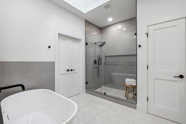 bathroom featuring tile patterned flooring, separate shower and tub, tile walls, and a skylight