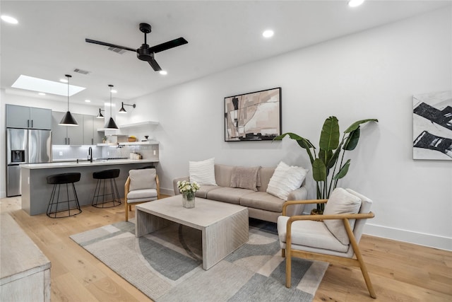 living room with light hardwood / wood-style flooring, ceiling fan, and sink