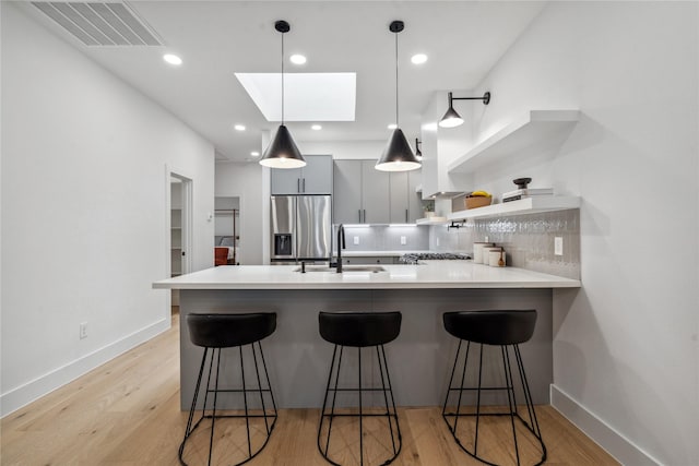 kitchen featuring sink, a kitchen breakfast bar, kitchen peninsula, stainless steel fridge, and light hardwood / wood-style floors