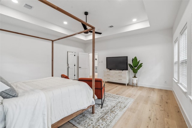 bedroom with light wood-type flooring and a tray ceiling