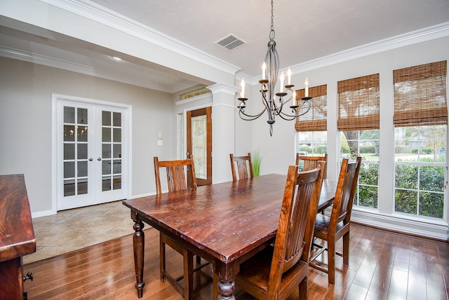 dining space featuring hardwood / wood-style floors, decorative columns, french doors, ornamental molding, and a chandelier