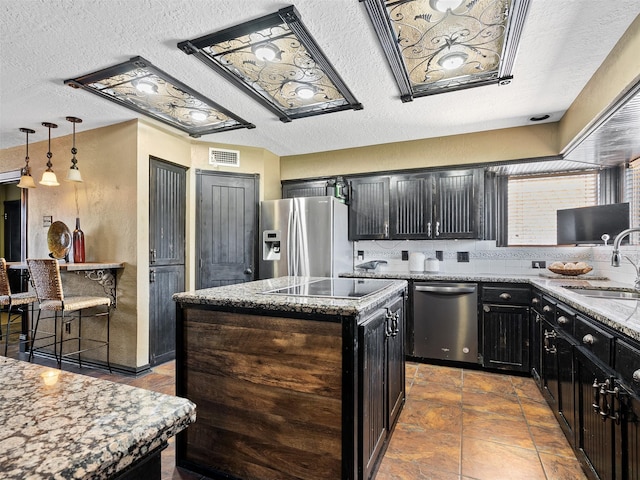 kitchen with hanging light fixtures, sink, a textured ceiling, appliances with stainless steel finishes, and a kitchen island