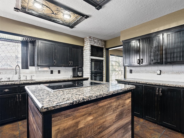 kitchen featuring a center island, backsplash, sink, light stone counters, and electric stovetop