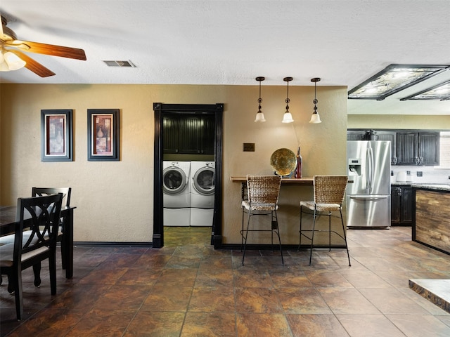 kitchen featuring ceiling fan, decorative light fixtures, washing machine and clothes dryer, stainless steel fridge with ice dispenser, and a breakfast bar area