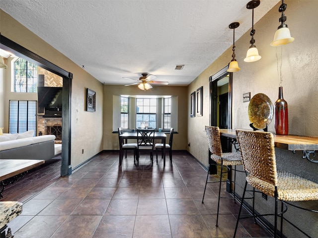 tiled dining area with a fireplace, ceiling fan, plenty of natural light, and a textured ceiling