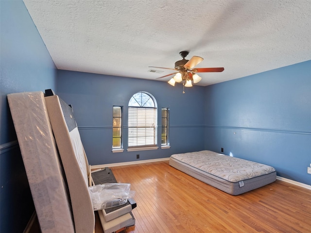 bedroom featuring ceiling fan, hardwood / wood-style floors, and a textured ceiling