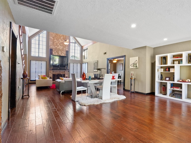 living room featuring a textured ceiling, dark hardwood / wood-style flooring, high vaulted ceiling, and a tiled fireplace