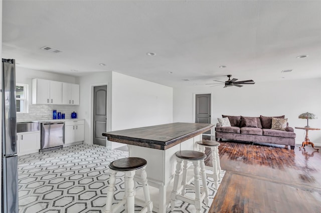 kitchen featuring ceiling fan, stainless steel appliances, backsplash, a breakfast bar, and white cabinets