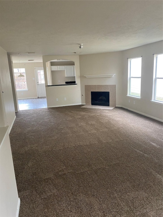 unfurnished living room with carpet flooring, a textured ceiling, and a tiled fireplace