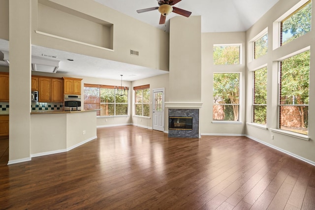 unfurnished living room with a premium fireplace, a towering ceiling, a healthy amount of sunlight, and dark hardwood / wood-style floors