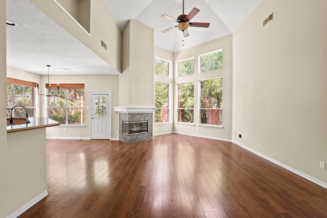 unfurnished living room featuring hardwood / wood-style floors, a high end fireplace, ceiling fan with notable chandelier, a towering ceiling, and a textured ceiling