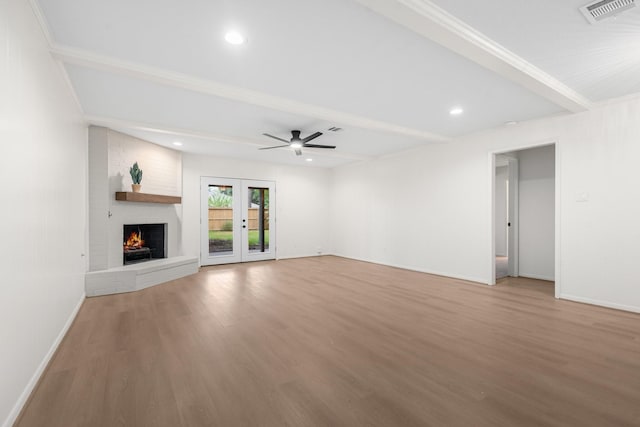 unfurnished living room with french doors, a brick fireplace, ceiling fan, beamed ceiling, and wood-type flooring