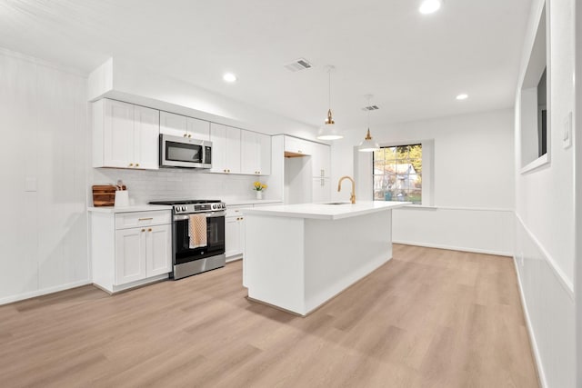 kitchen featuring light hardwood / wood-style flooring, decorative light fixtures, a center island with sink, white cabinets, and appliances with stainless steel finishes