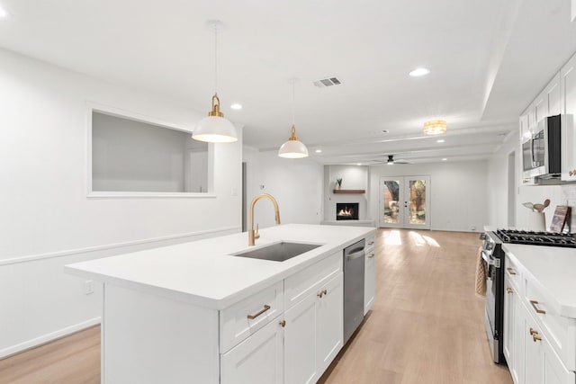 kitchen with sink, an island with sink, decorative light fixtures, white cabinets, and appliances with stainless steel finishes