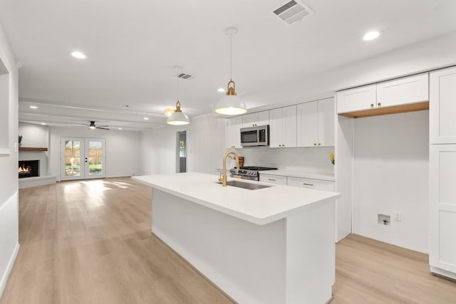 kitchen with sink, decorative light fixtures, light hardwood / wood-style flooring, a center island with sink, and white cabinets