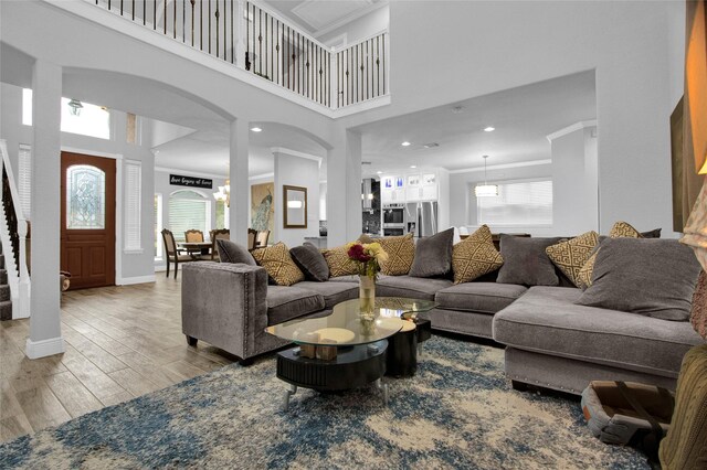 living room with crown molding, a towering ceiling, a chandelier, and light wood-type flooring